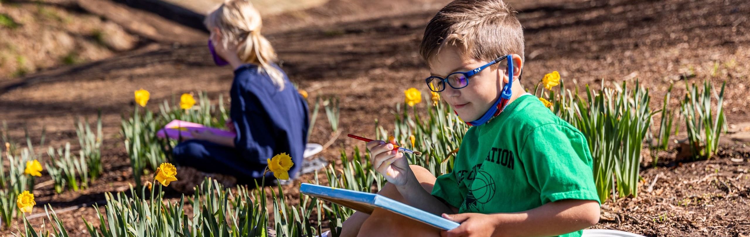 Two children sitting in amongst grass whilst painting